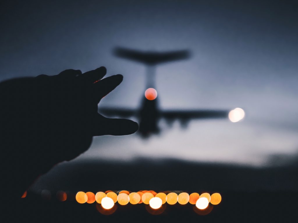 Silhouette photo of a hand reaching out to a landing plane