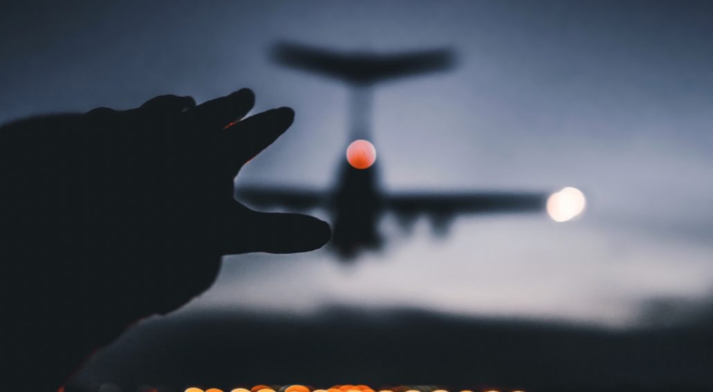 Silhouette photo of a hand reaching out to a landing plane