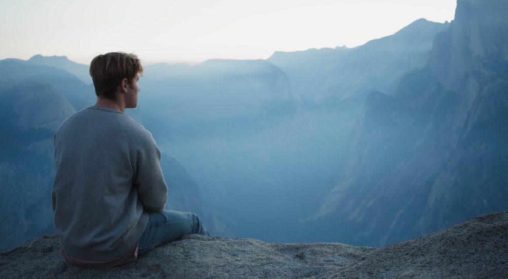 A man in gray shirt sitting on a cliff