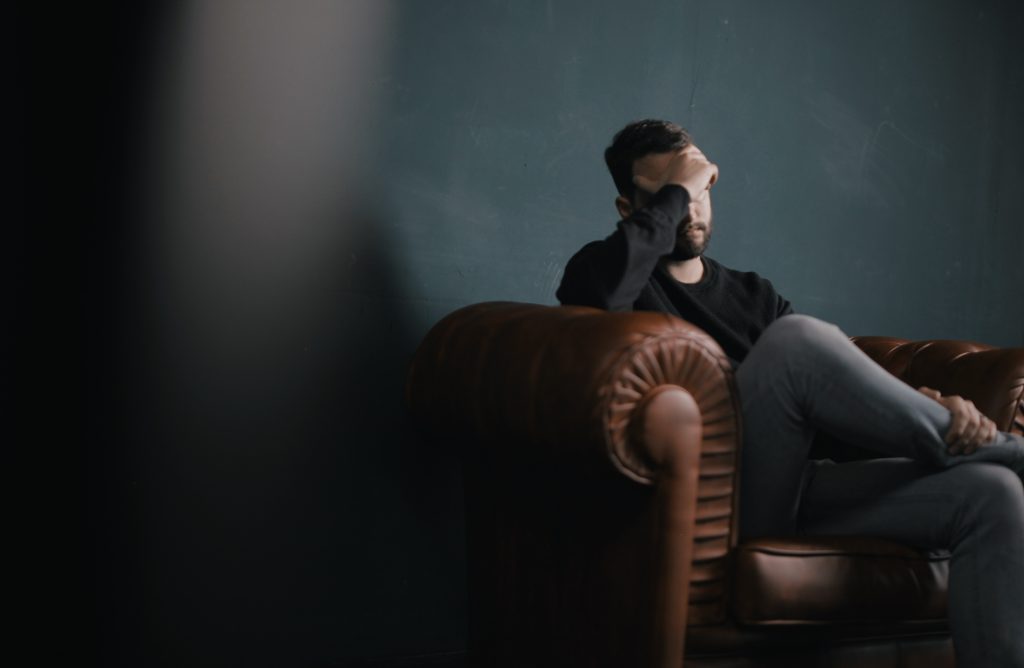 Man holding his head while sitting on a sofa