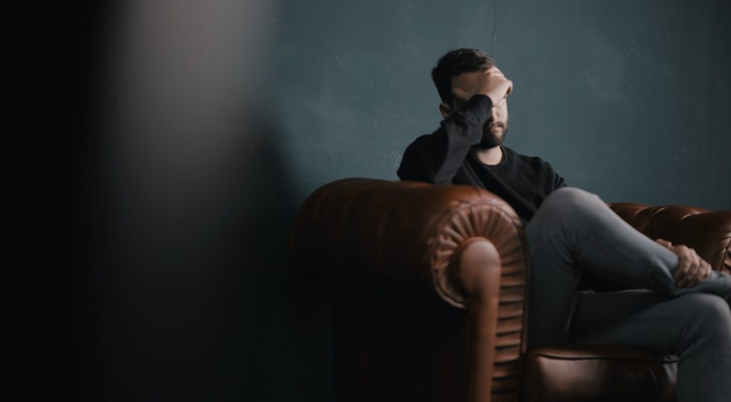 Man holding his head while sitting on a sofa