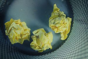 Three yellow crumpled papers in a gray trash bin