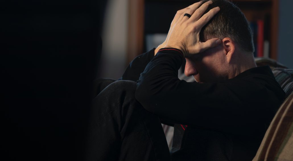 A man sitting in a couch holding his head in his hands