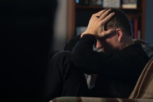 A man sitting in a couch holding his head in his hands