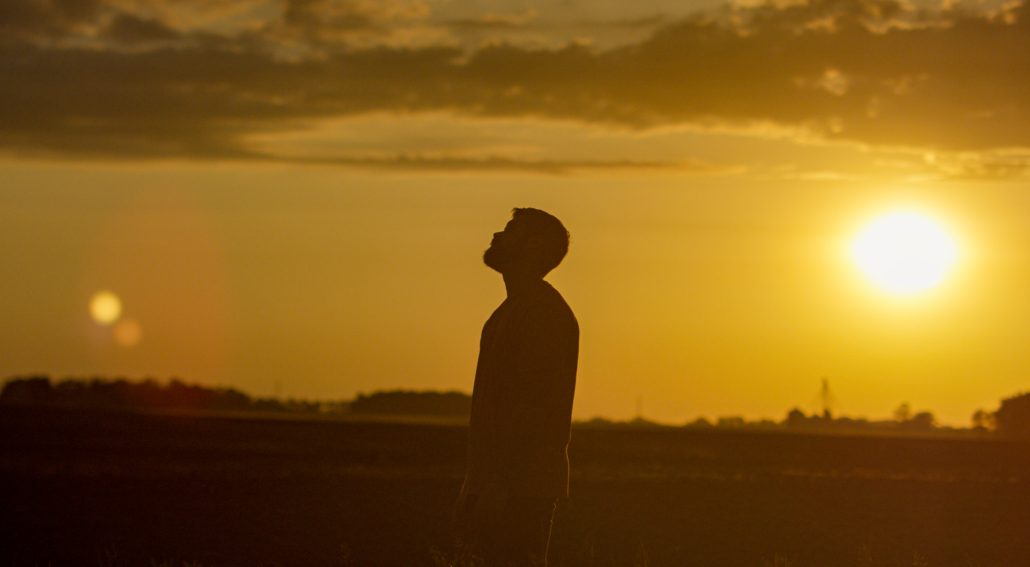 Silhouette of a person standing on a filed during sunset