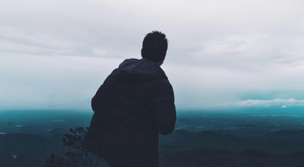 A man standing on top of a mountain staring at the aerial view