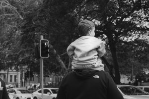 Child sitting on an adult’s shoulders at a city crosswalk.