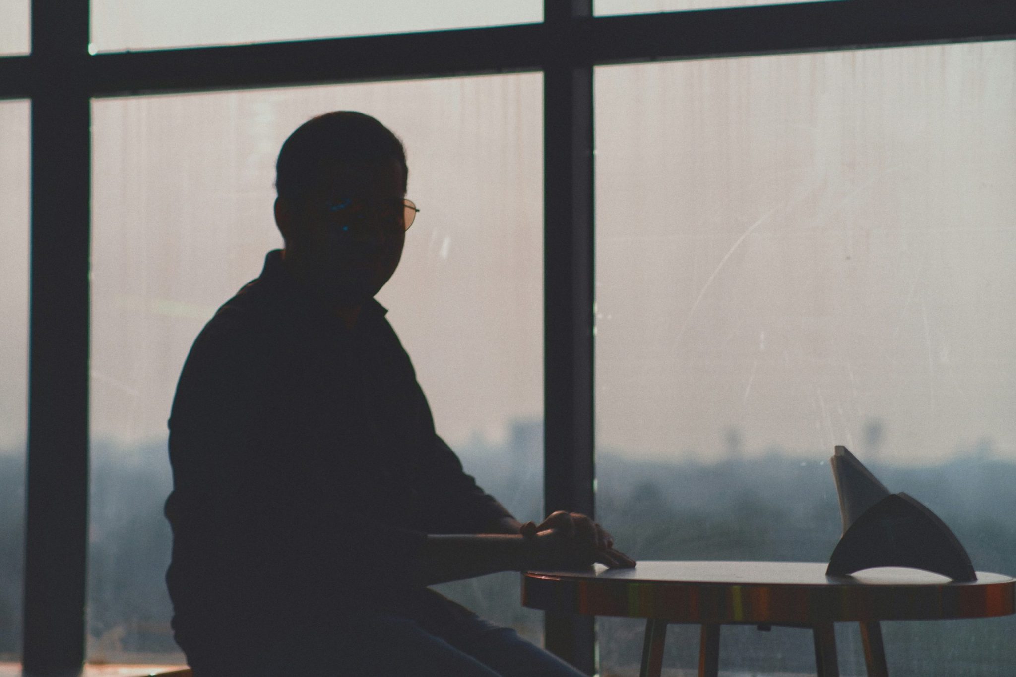 Silhouette of a person sitting at a small table near a large window