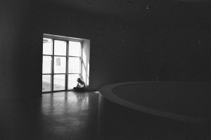 A man sitting beside a large window in a dark room