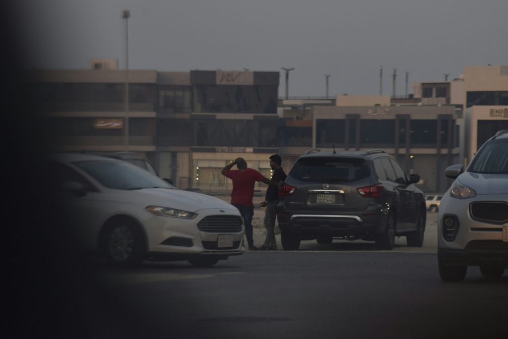 People talking between parked cars with buildings in the background