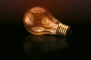 A glowing light bulb lying on a dark reflective surface