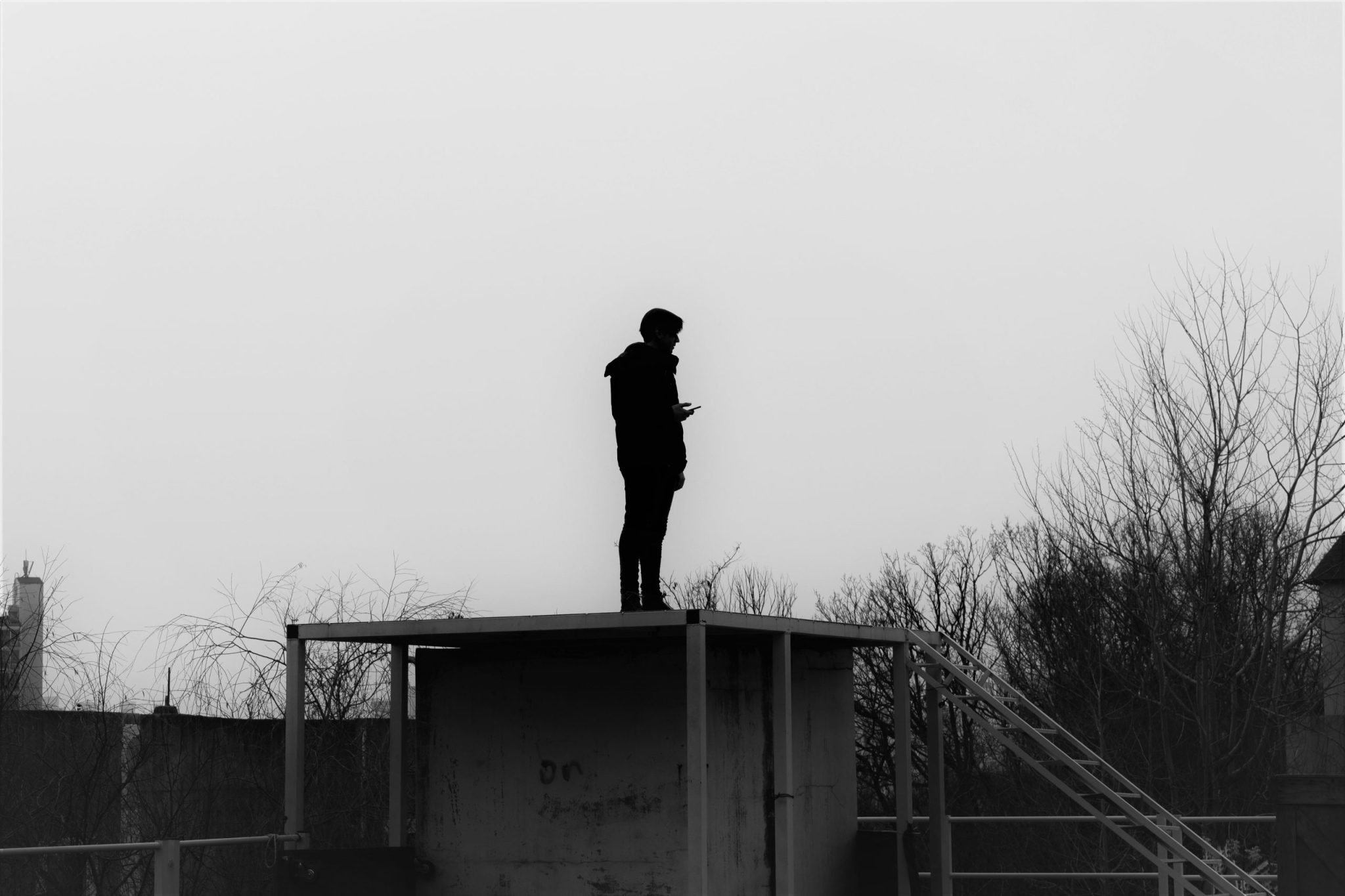 Silhouette of a person standing on a rooftop structure against an overcast sky
