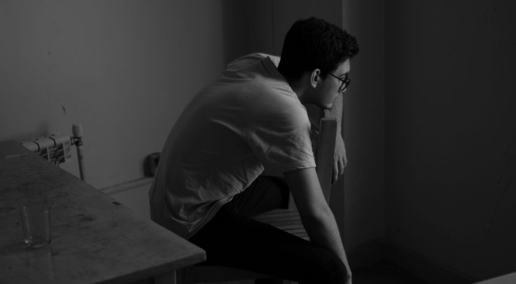 Person sitting on a chair, leaning forward in a dimly lit room