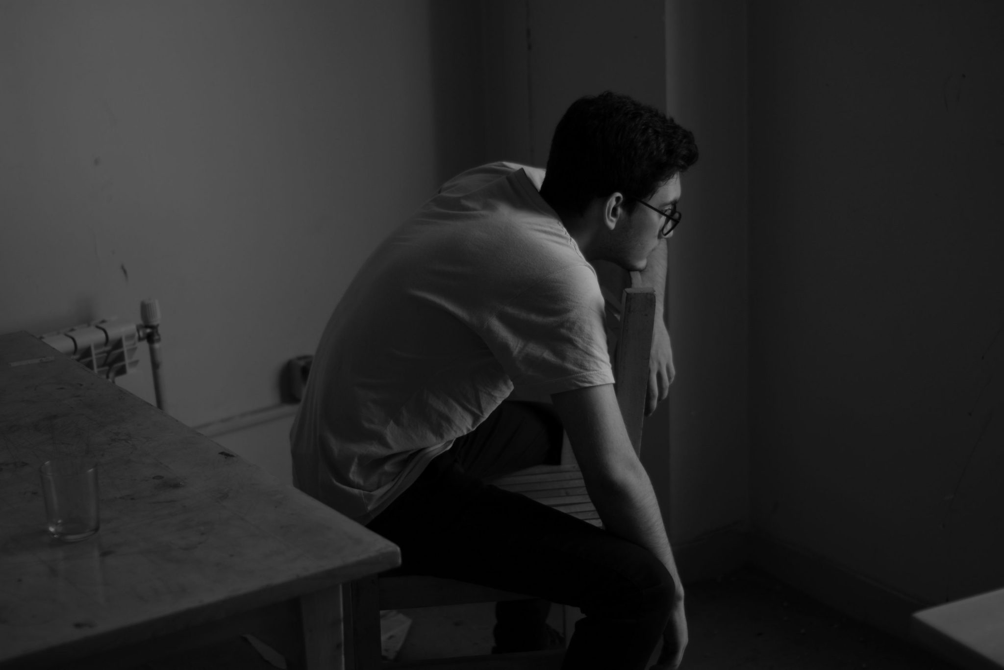 Person sitting on a chair, leaning forward in a dimly lit room