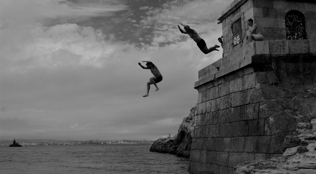 People jumping off a stone structure into the sea