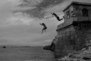 People jumping off a stone structure into the sea