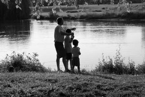 A dad fishing with two children by a calm lakeshore.