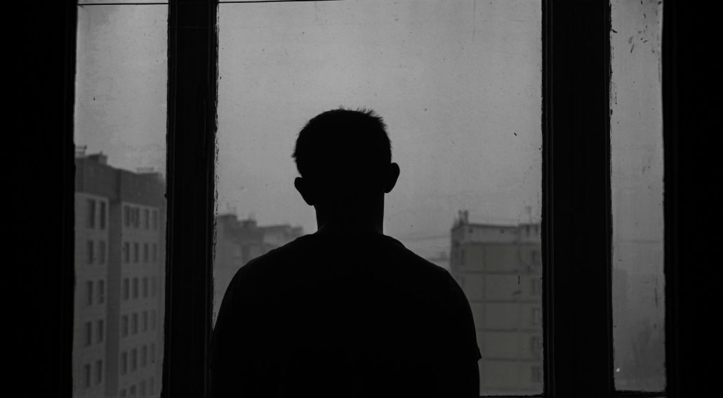 Silhouette of a person standing and looking out a large window