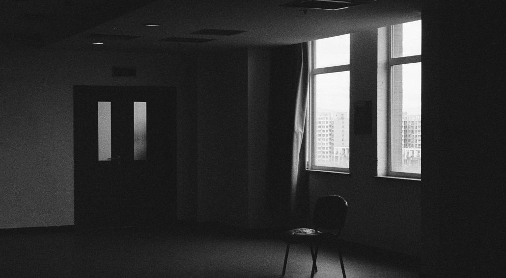 A lone chair in a dimly lit room with windows