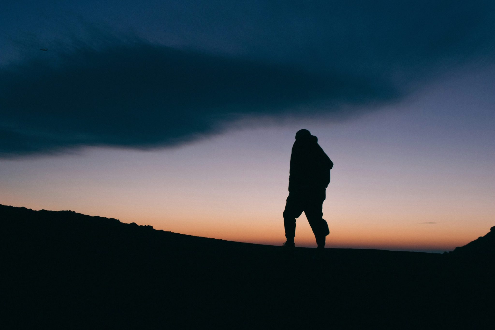 Silhouette of a man on top of a mountain at dusk