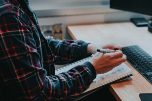 Person writing notes in a planner beside a keyboard at a desk