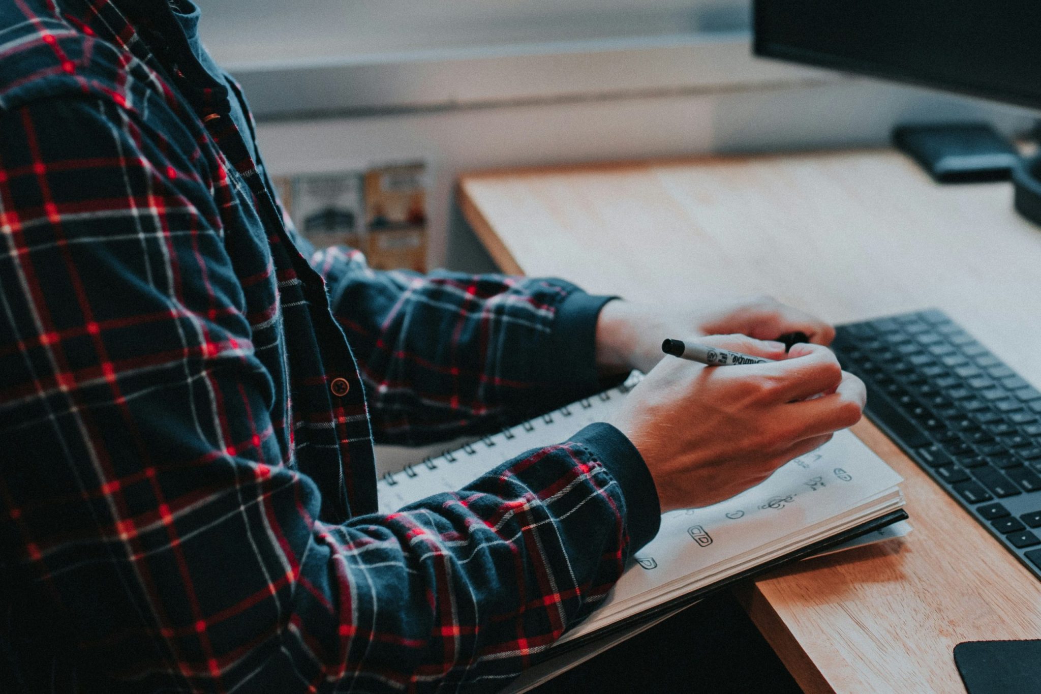 Person writing notes in a planner beside a keyboard at a desk