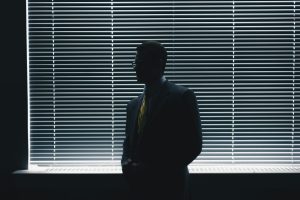Silhouette of a man in suit standing near window blinds