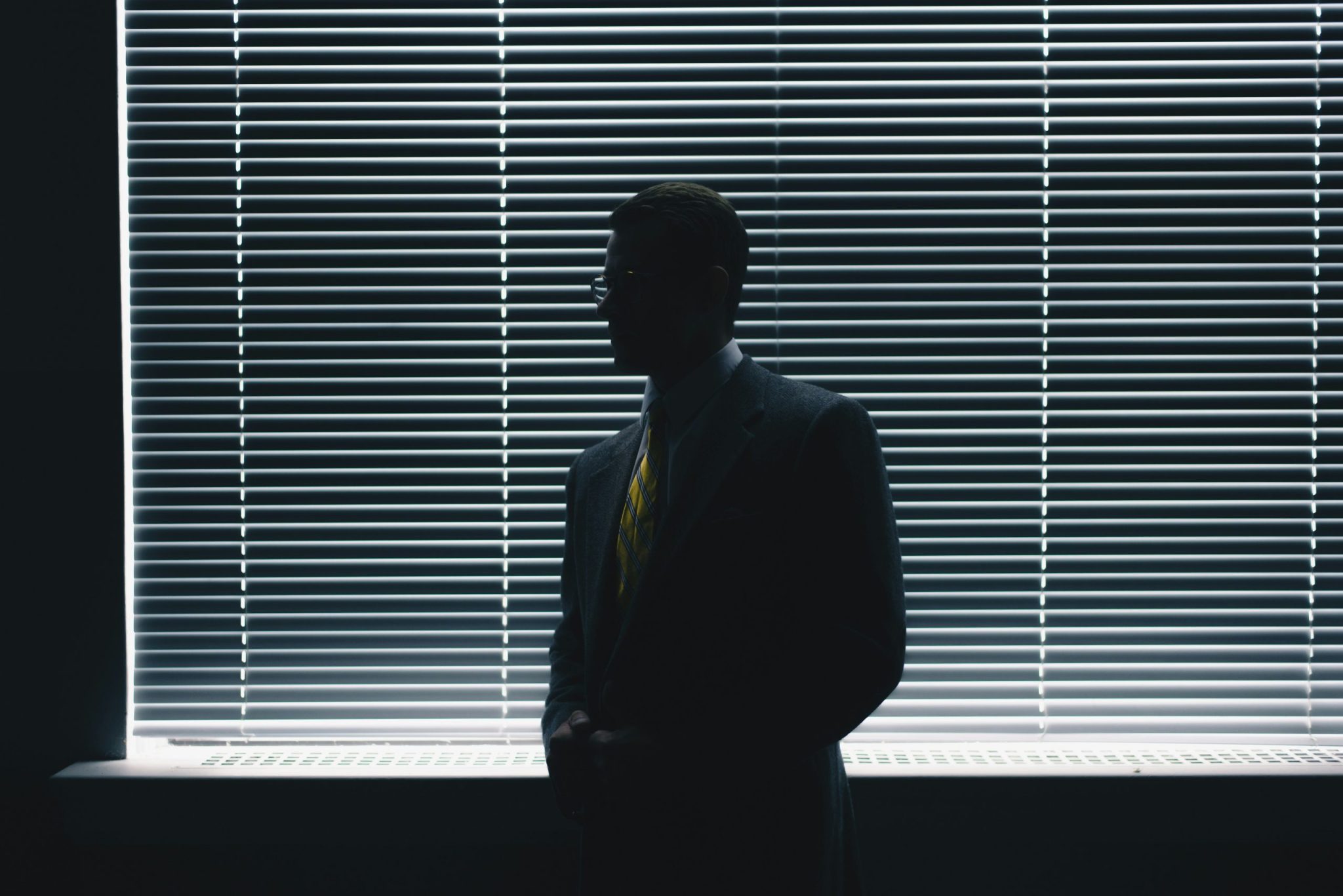 Silhouette of a man in suit standing near window blinds