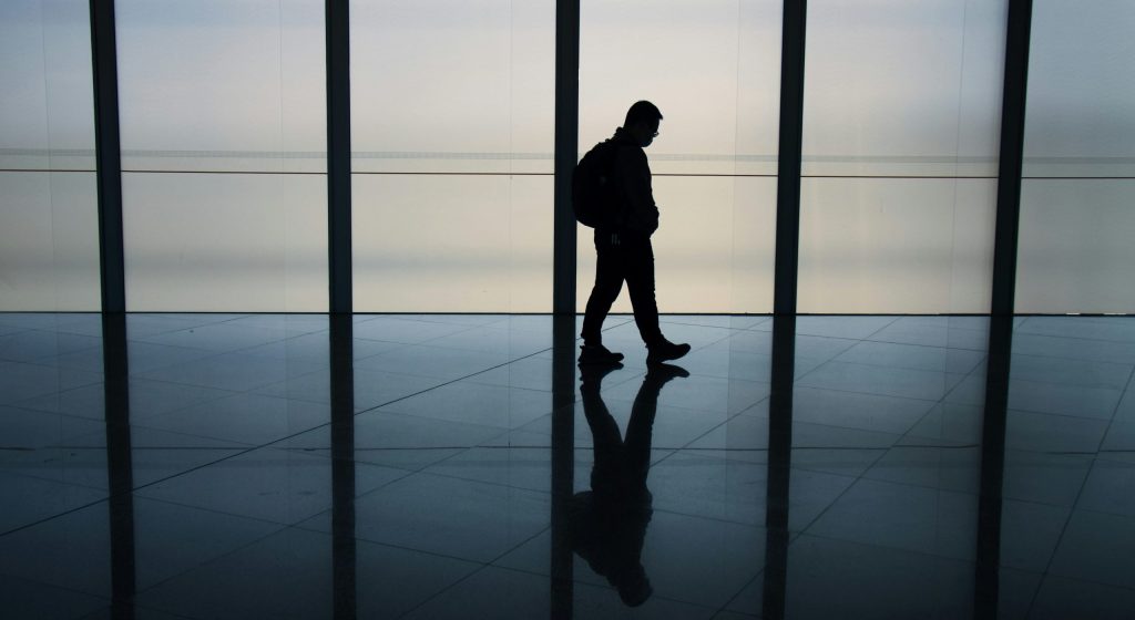 Silhouette of a lone person walking through a spacious, modern corridor, reflecting on the polished floor
