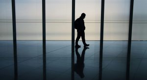 Silhouette of a lone person walking through a spacious, modern corridor, reflecting on the polished floor
