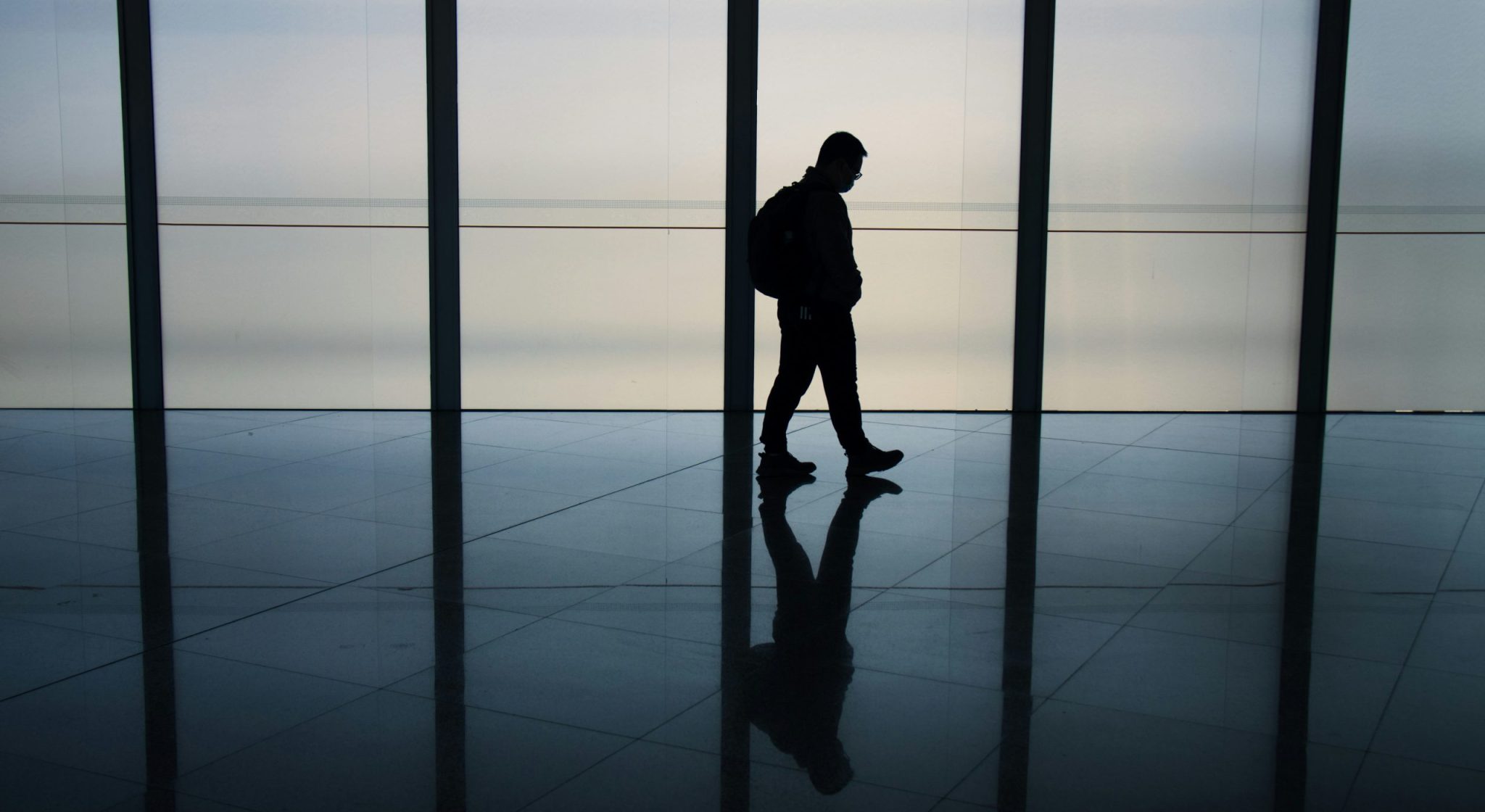 Silhouette of a lone person walking through a spacious, modern corridor, reflecting on the polished floor