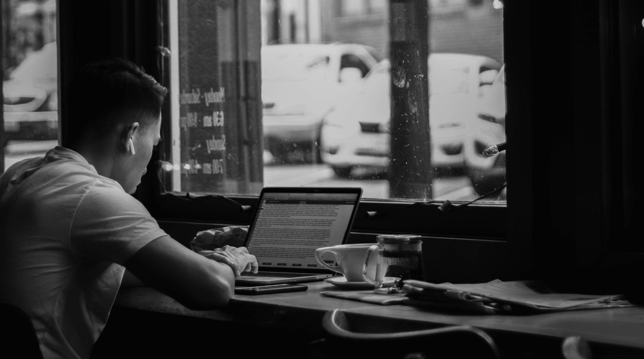 Black and white photo of a man working on his laptop in a cafe