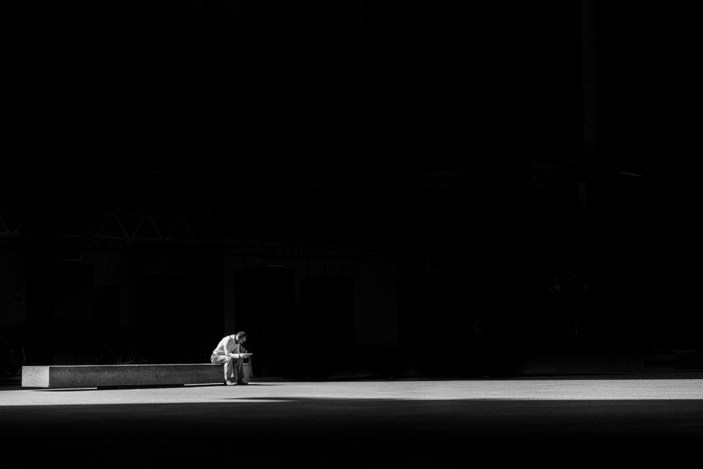 Grayscale photo of a man sitting on a concrete bench