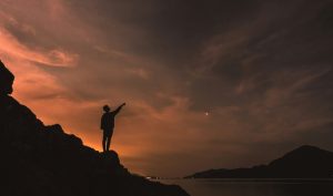 Silhouette of a person standing on top of the mountain with an overlooking sea view