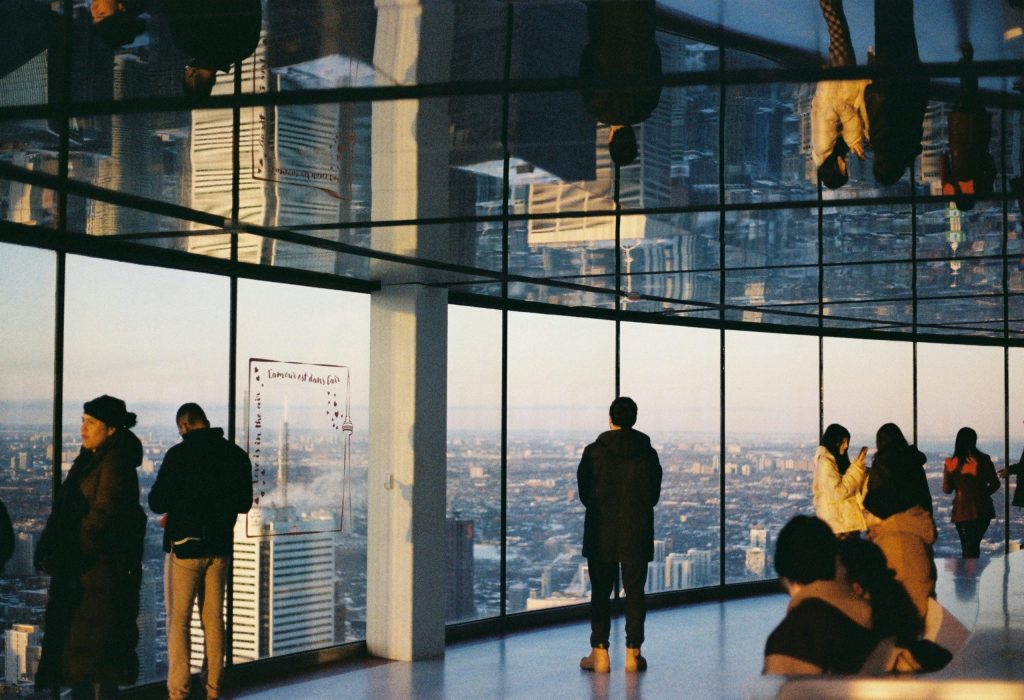 Photo of people admiring the city view through the wide glass window of a building