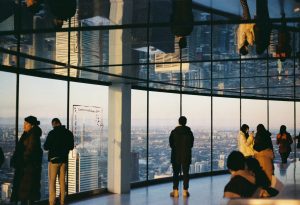 Photo of people admiring the city view through the wide glass window of a building
